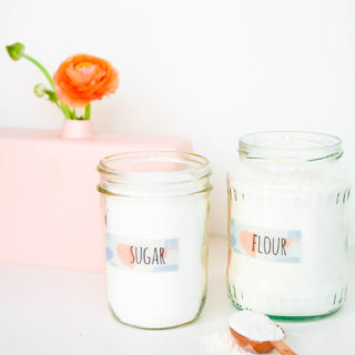 Watercolor Pantry Labels on two mason jars filled with flour and sugar with a tablespoon of flour on the counter and a flower and vase in the background