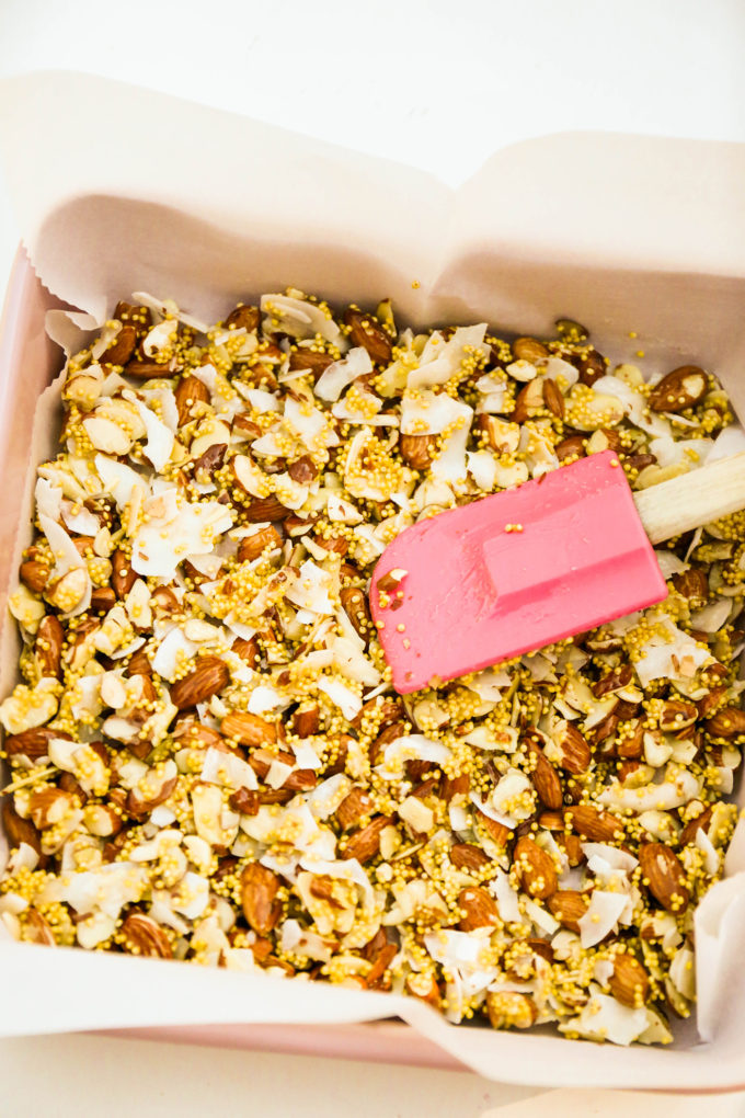 granola bar ingredients spread in baking pan with pink spatula 