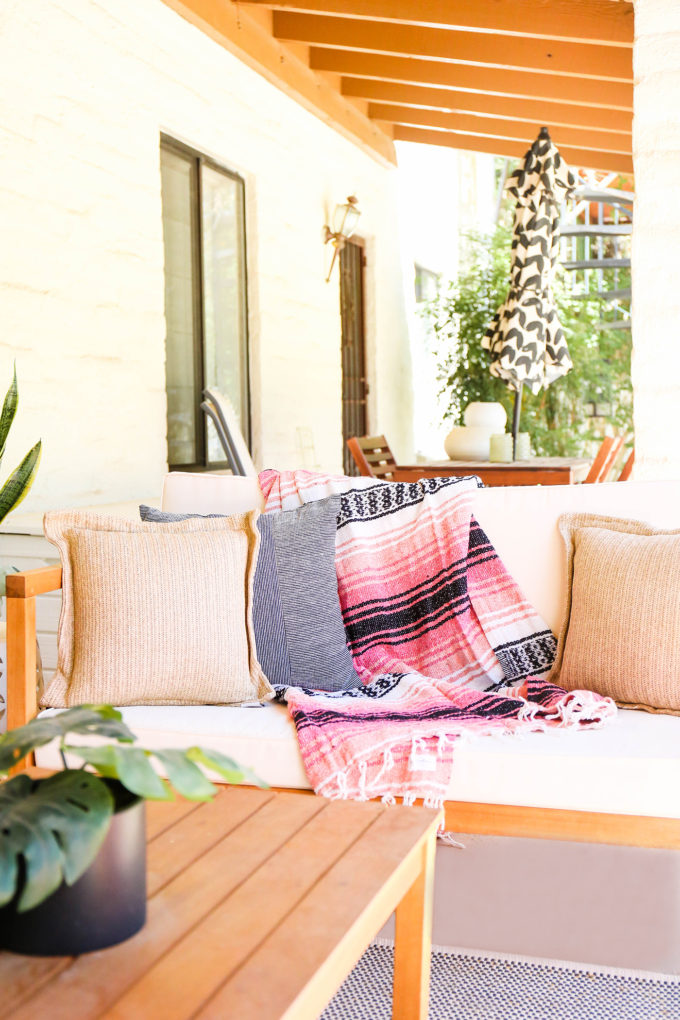 mexican blanket rests on modern white outdoor loveseat with throw pillow