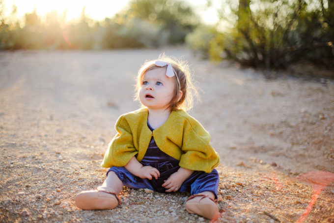 baby girl sitting in sand in desert at sunset