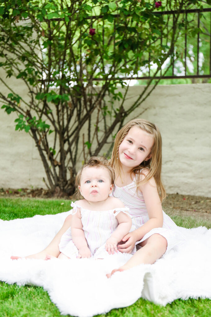 sisters sitting in easter dresses posing on grass 