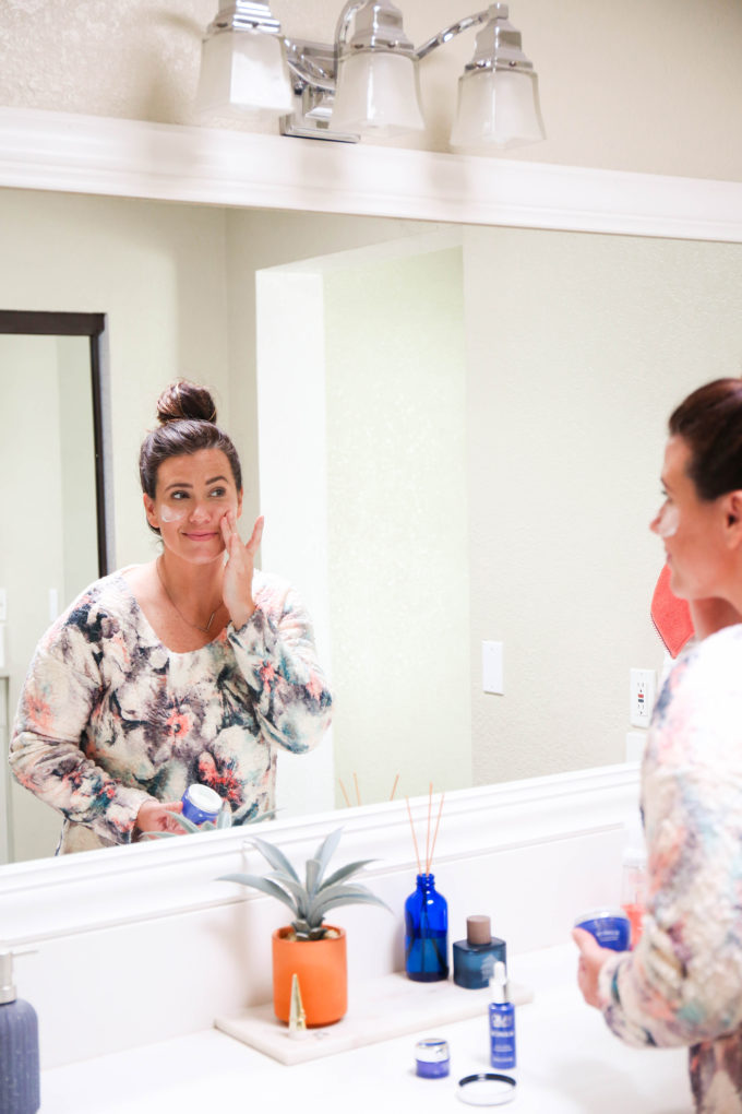 woman applying moisturizer in bathroom mirror 