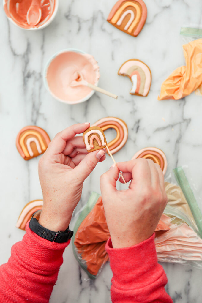 hands holding a cookie and toothpick designing frosting 