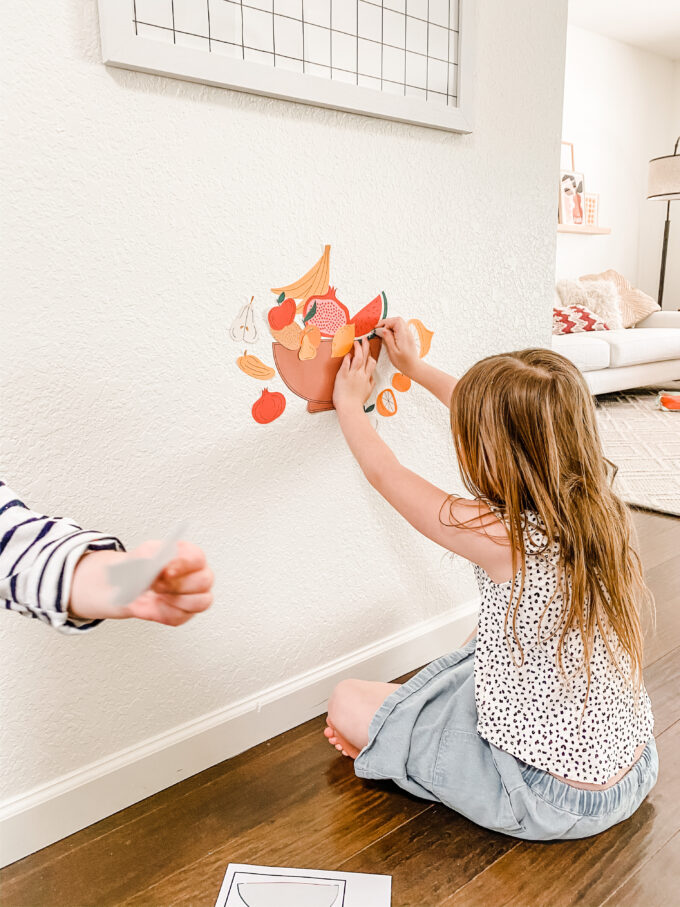 little girl placing fruit stickers on wall 