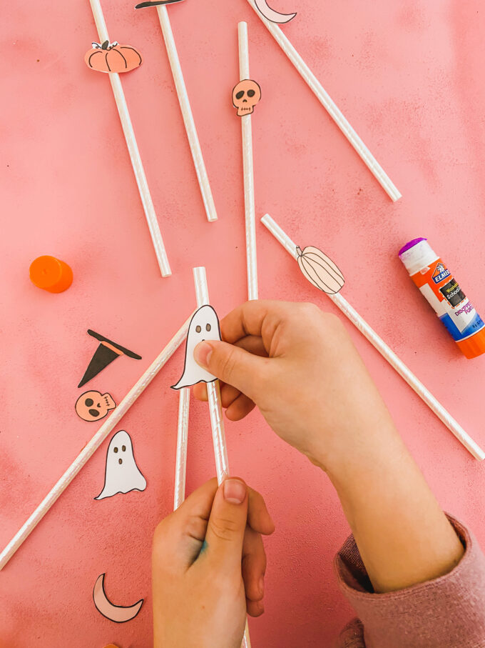 little girl hands glueing halloween printables to straws 